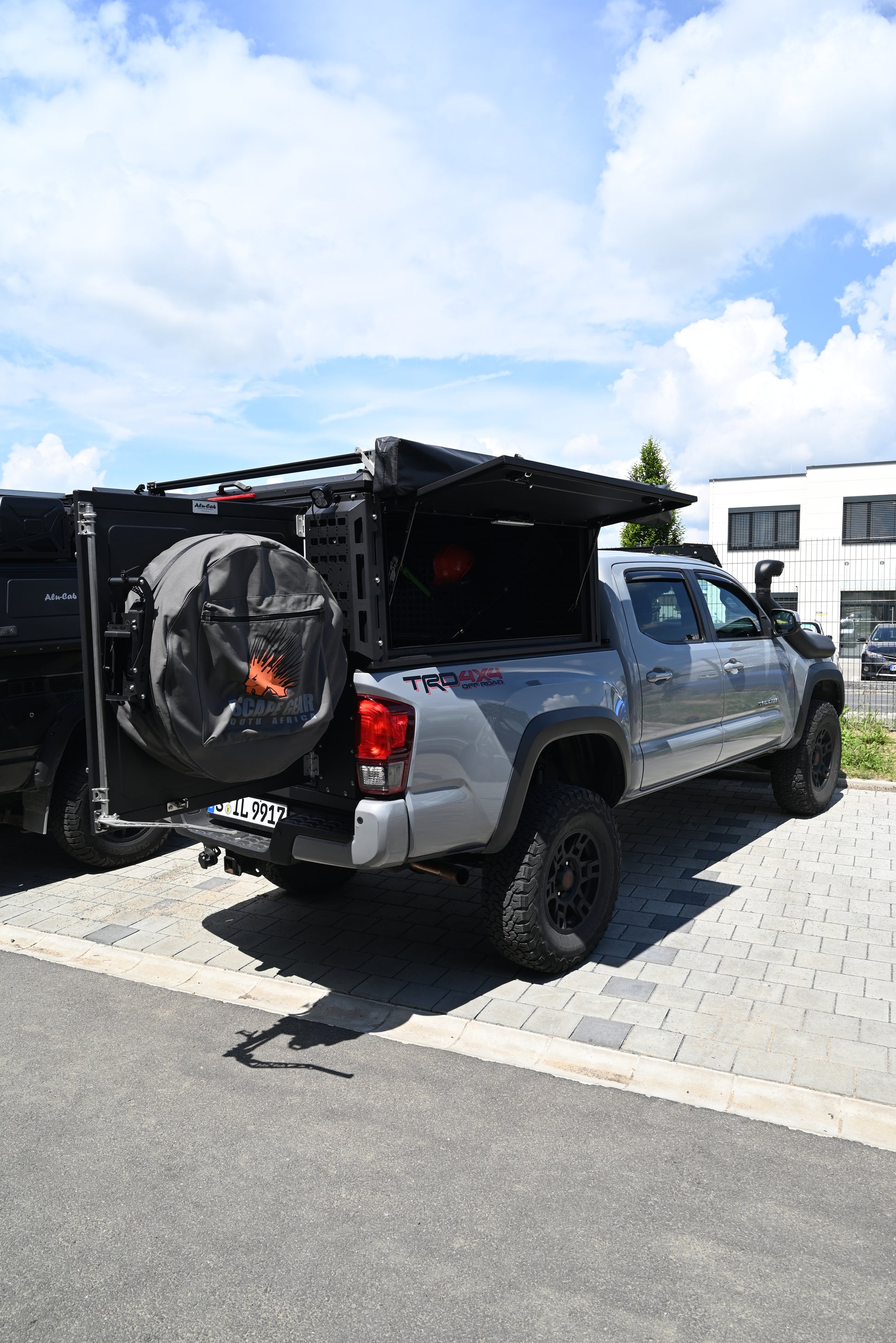 ModCAP Worker zu sehen. Montiert auf einem Offroad Fahrzeug. Mit geöffneter Hecktür und Seitentüren. Mit montiertem Ersatzrad, Lazerlamps und einer Markise.