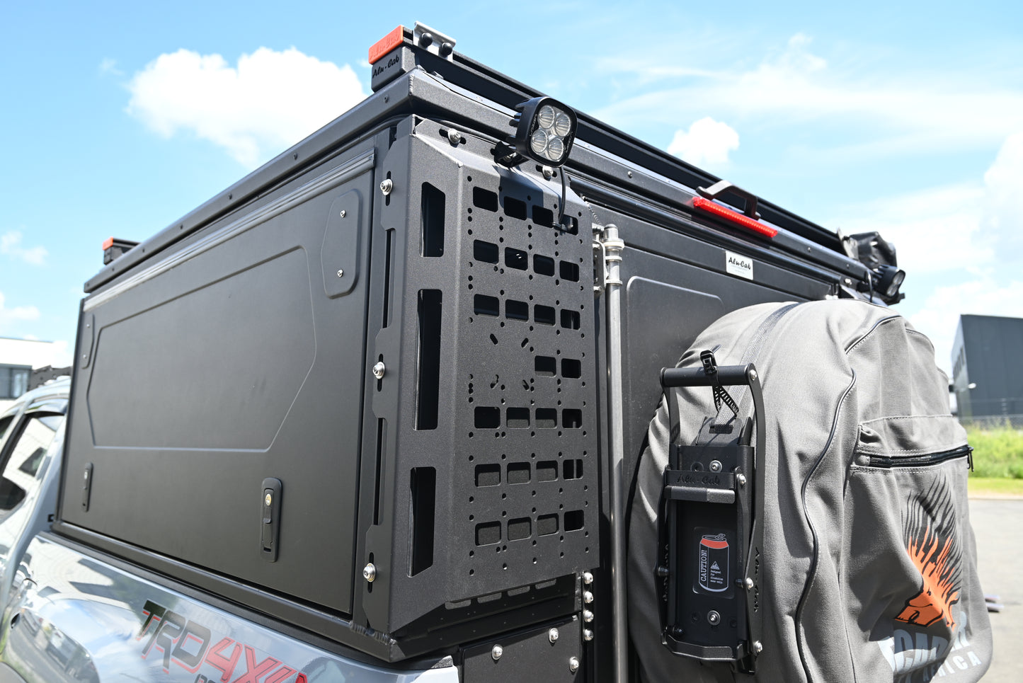 ModCAP Worker zu sehen. Montiert auf einem Offroad Fahrzeug. Mit Geschlossener Hecktür und Seitentüren. Blick auf die Molleplatte neben der Hecktür. Mit montiertem Ersatzrad, Lazerlamps und einem Can Crusher.